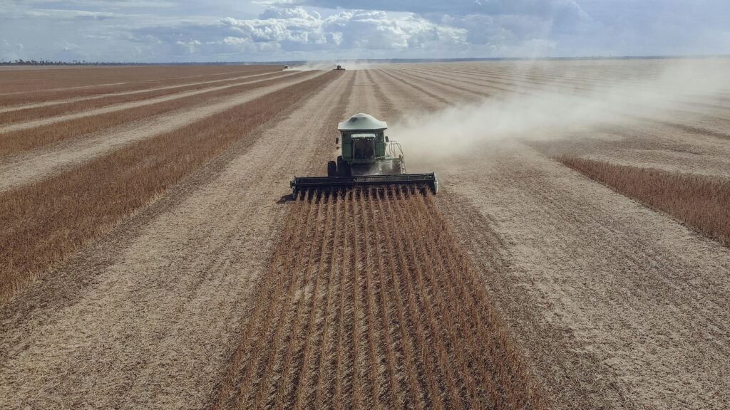 Aerial view of a combine harvester working in a vast soybean field under a cloudy sky.